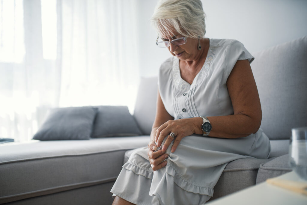 Mulher idosa sentada no sofá com dores no joelho